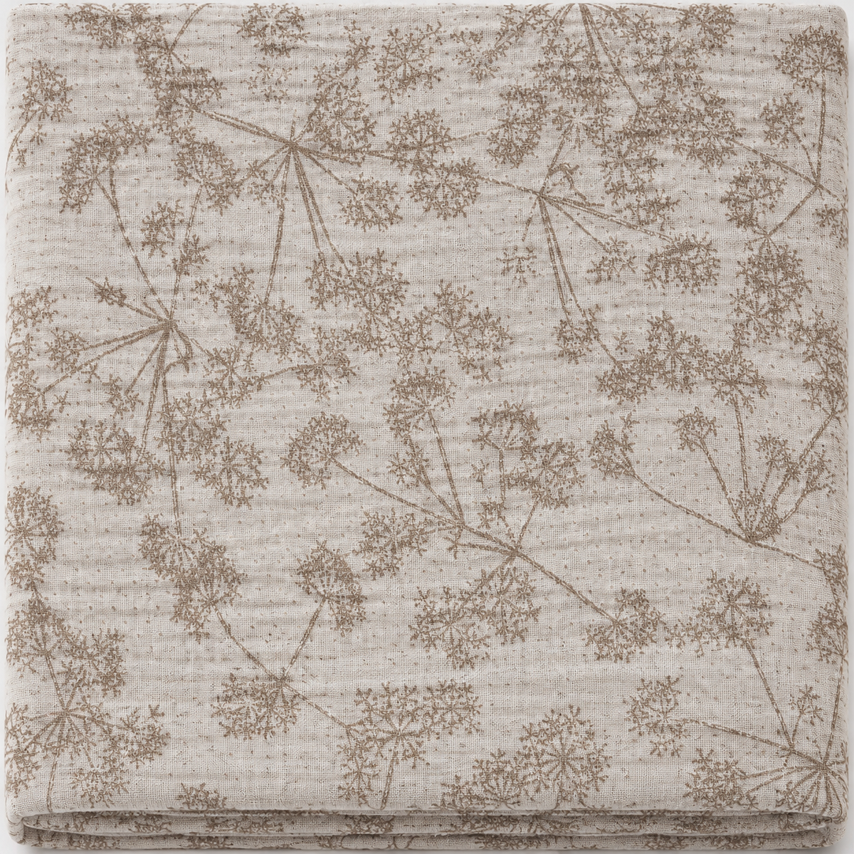 A folded cotton muslin cloth featuring a delicate brown botanical pattern of dandelion-like flowers on a warm beige textured background.