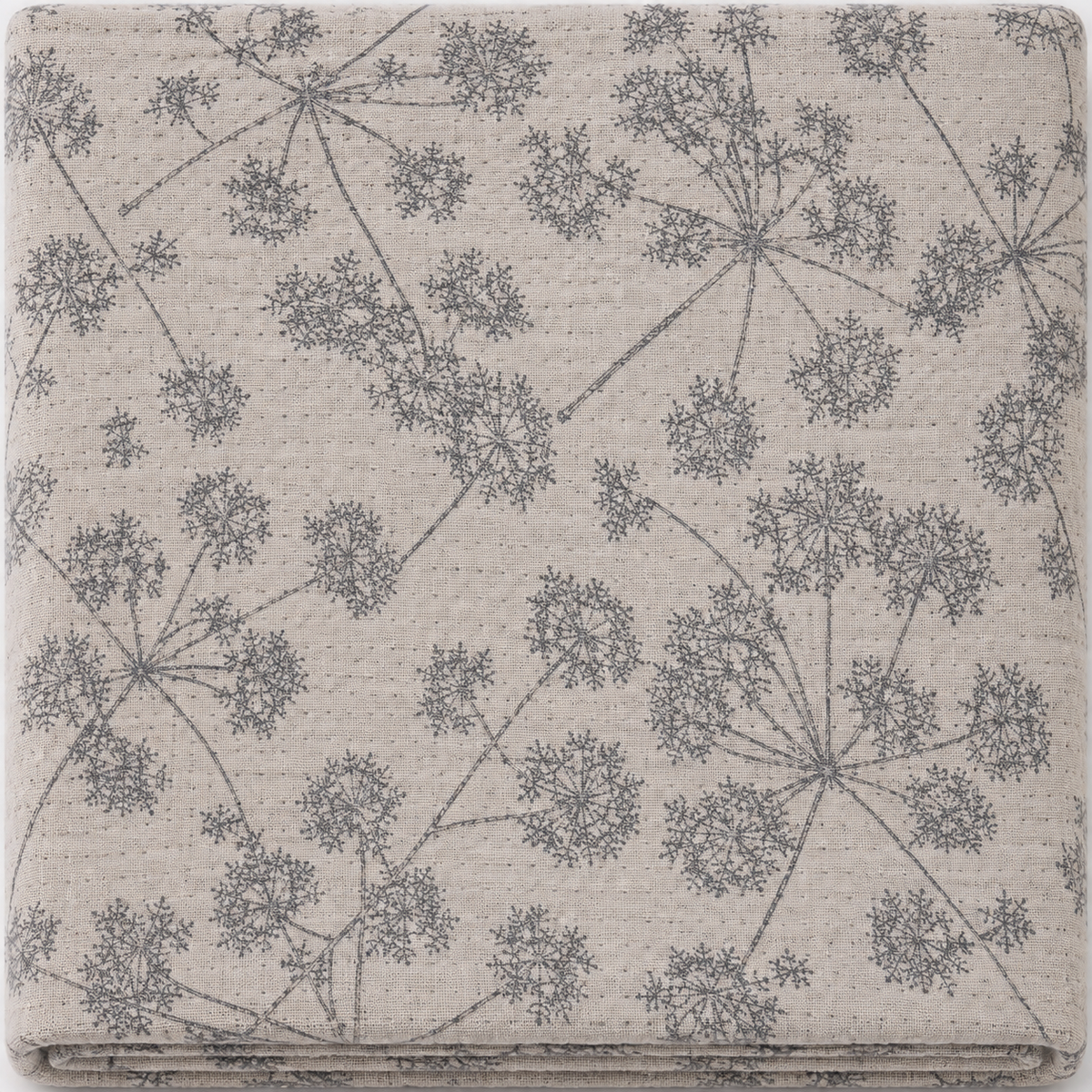 A folded textile item, likely a blanket or throw, featuring a gray dandelion-like botanical pattern on a textured beige background.