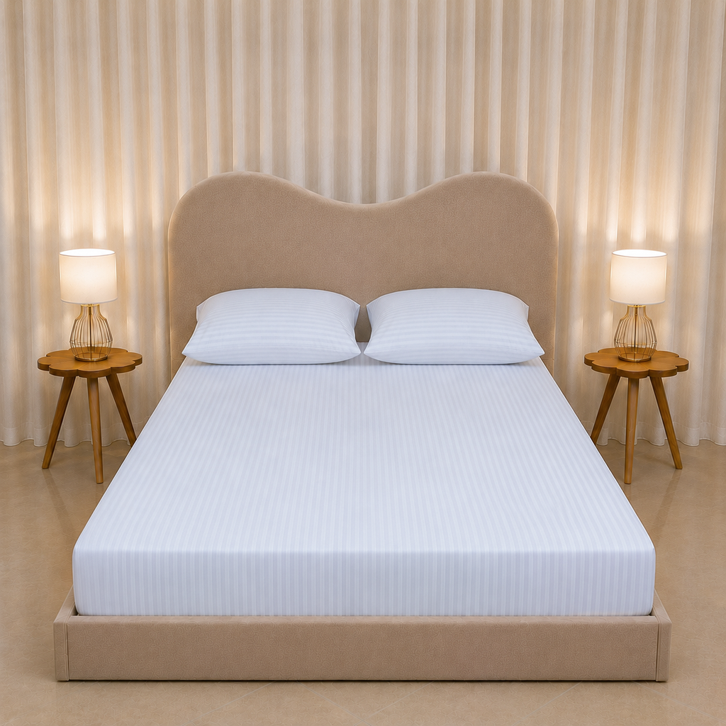 A neatly made bed with a white striped mattress cover and two white pillows, set in a modern bedroom with a beige upholstered headboard and footboard, flanked by two wooden side tables with lit lamps against a beige curtain backdrop.