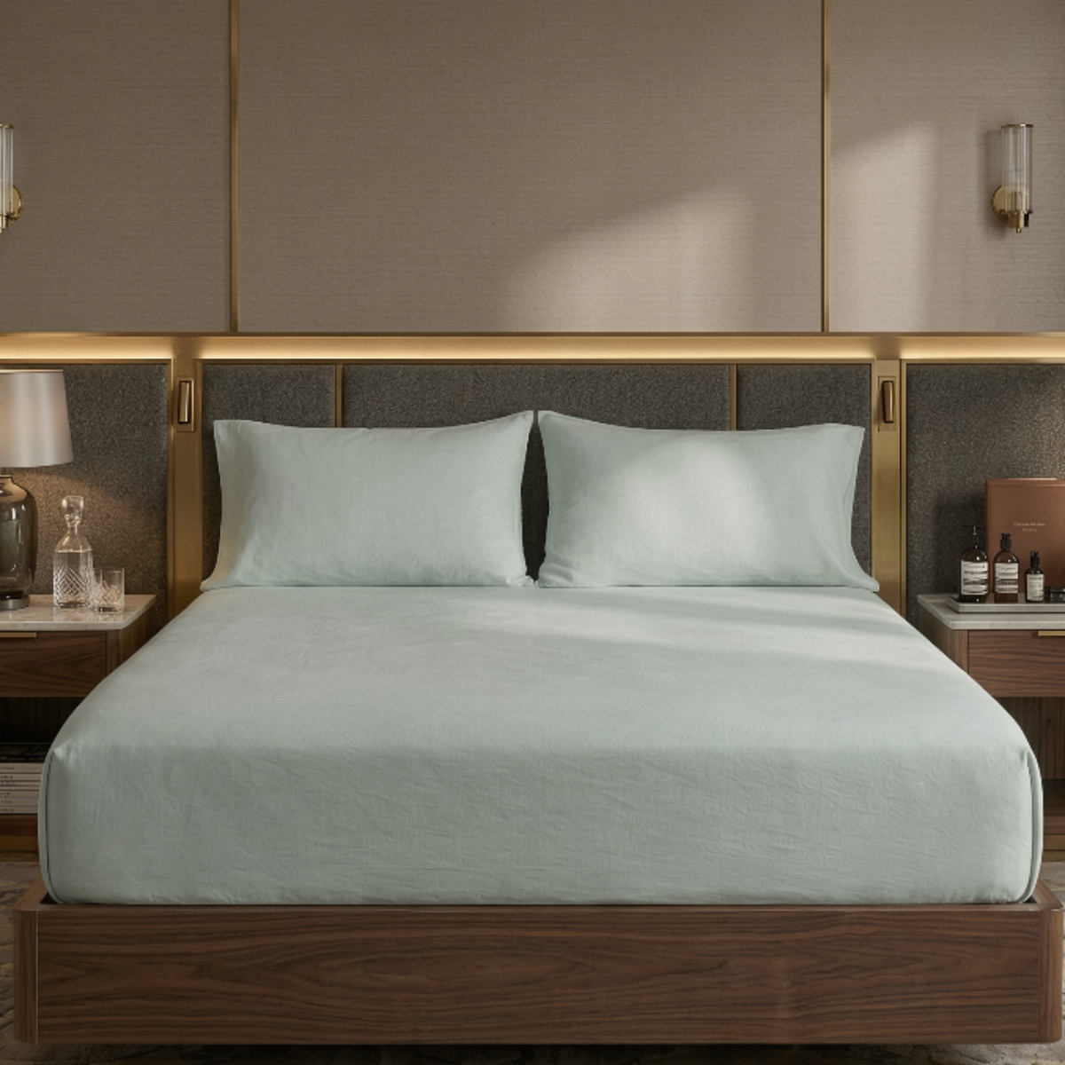 A modern wooden bed frame with a dark upholstered headboard and gold trim, dressed in pale mint green bedding, set in a luxury bedroom with matching nightstands and a chair.